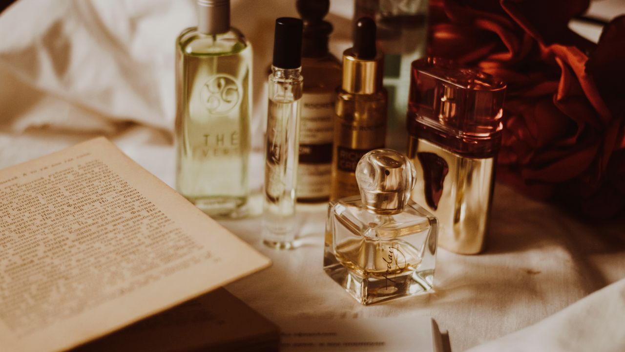 A still life of perfume bottles, an open book and a deep red drape